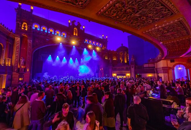 A busy music venue with an ornate stage and blue lights.
