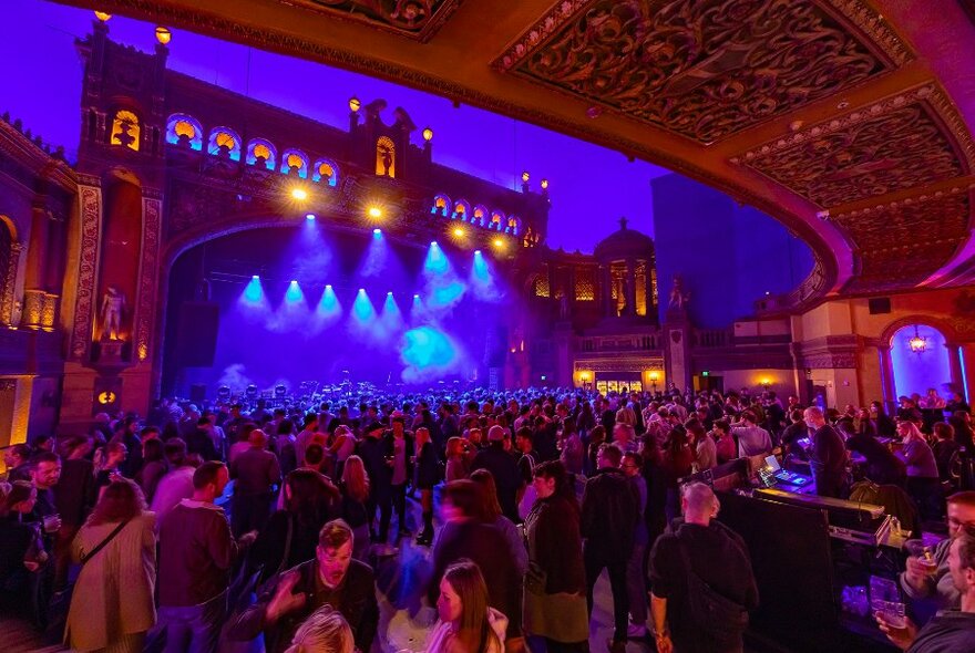 A busy music venue with an ornate stage and blue lights.