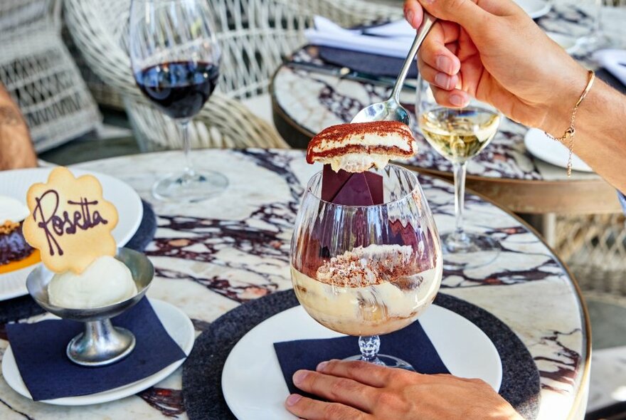 Someone taking a spoonful of tiramisu from a dessert glass at a restaurant.