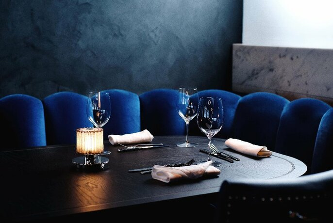 Interior of restaurant Grill Americano, with a dark wooden table set for a meal service, royal blue velvet banquette seating and soft lighting.