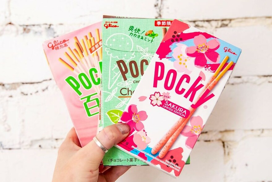 A hand holding three assorted flavours of Pocky snacks. 