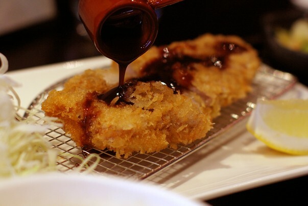A close up of tonkatsu with sauce being drizzled by a spoon over the top. 