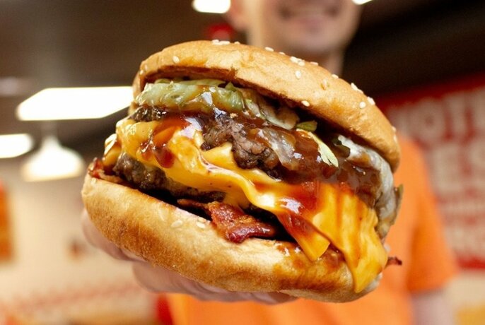 Person holding massive double-patty burger with all the fixings.
