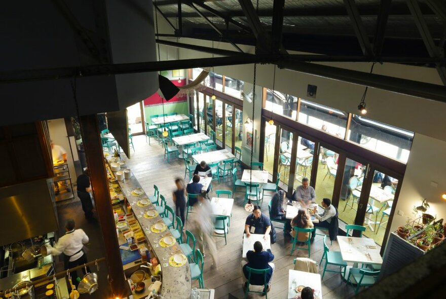 The inside of an Italian taverna looking down from the ceiling over the patrons, tables, chairs and bar.