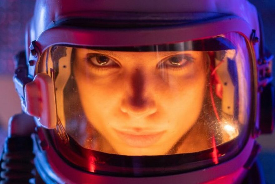 Person's face looking through a spacesuit helmet.