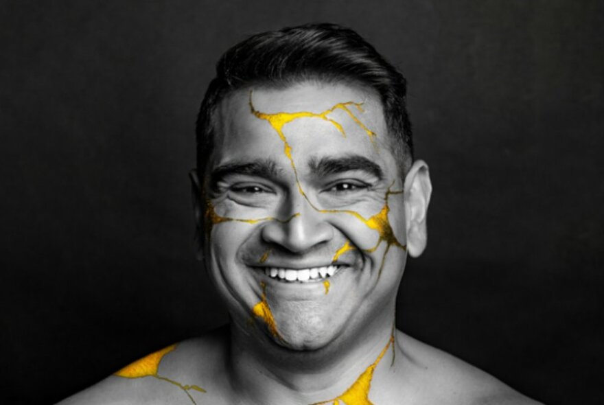 A black and white image of Dilruk Jayasinha smiling broadly while cracks of yellow appear over his face and body.