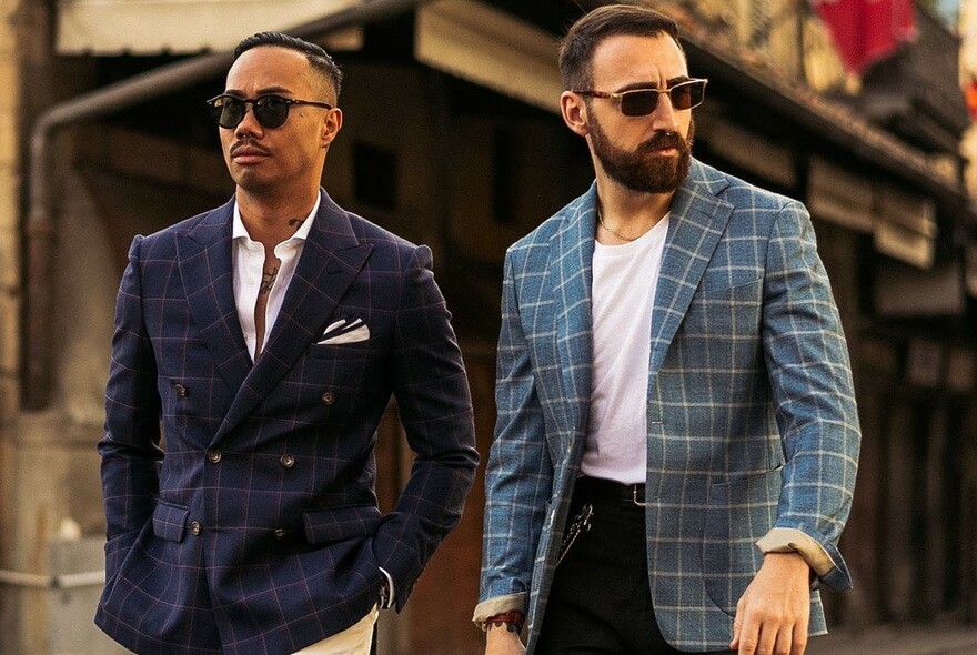 Two male models wearing plaid jackets and sunglasses.