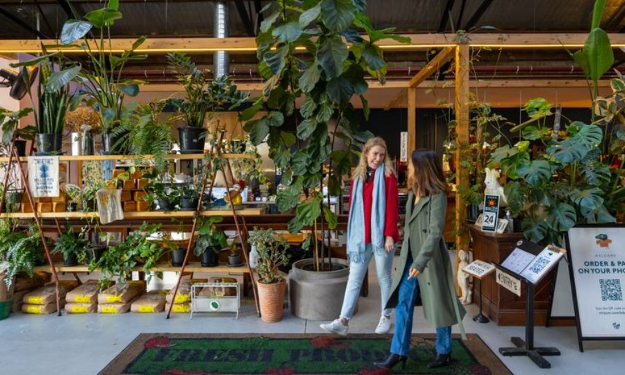 Two girls smiling at ear other as they walk out of cafe surrounded by indoor plants.