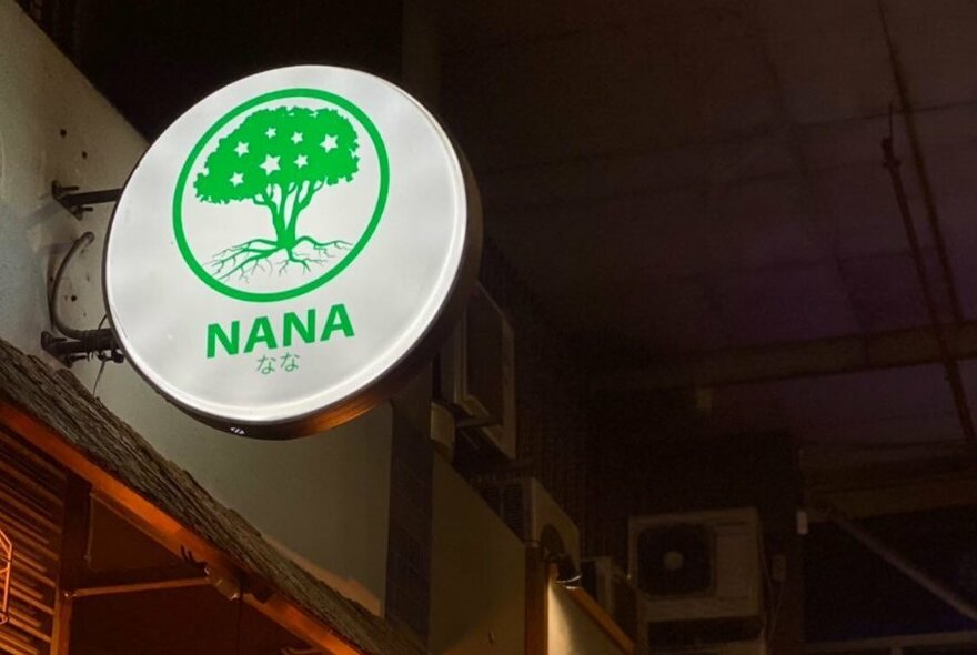Exterior of Nana, with white lit sign featuring green tree and word, Nana.