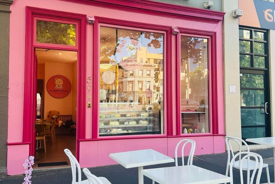 The bright pink shopfront of Yummy Bear Bakery, with white tables and chairs out the front.