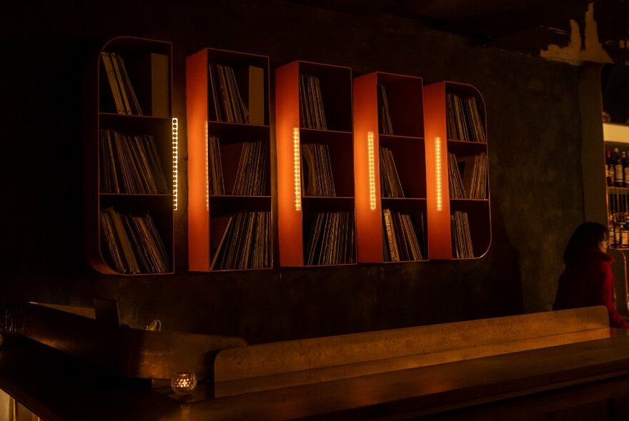 A wall of vinyl records in cube shelving, dimly lit.