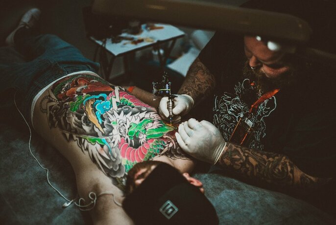 A tattoo artists working on a large back piece in a darkened room. 