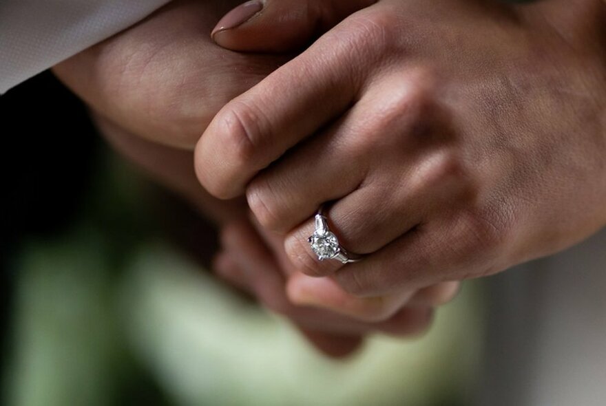 Clasped hands, a diamond ring on one of the fingers.