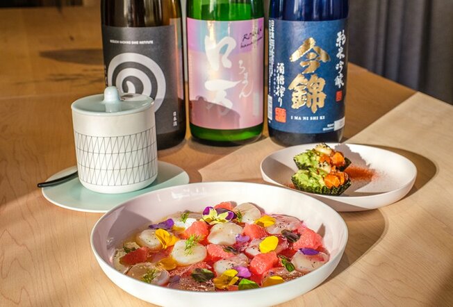A colourful Japanese dish in a restaurant with three bottles of sake. 