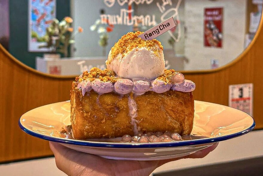 A hand holding a dessert plate with a cake topped with ice cream.