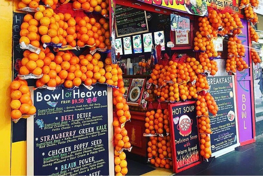 Close up of shopfront, with bags of oranges and blackboard menus around entrance.