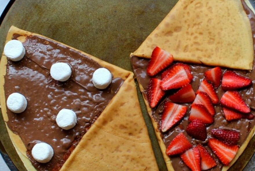 Two large folded over crepes, one with melted chocolate and fresh strawberries, the other with chocolate and marshmallows.