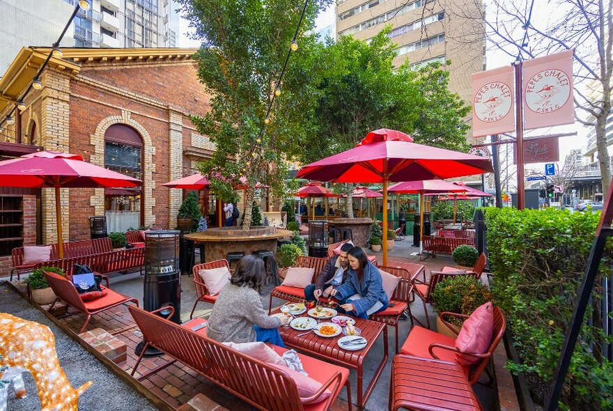 A group dining on red benches in an outdoor beer garden.