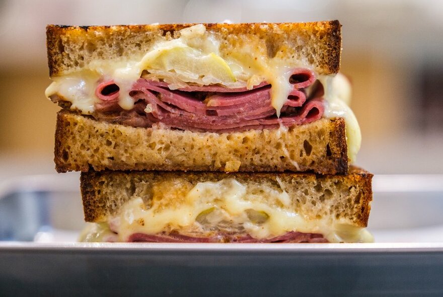 Two halves of a sliced Reuben sandwich with thick layers of meat and melting cheese.