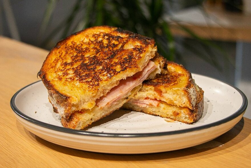 A ham and cheese toasted sourdough sandwich cut in half on a natural coloured plate.