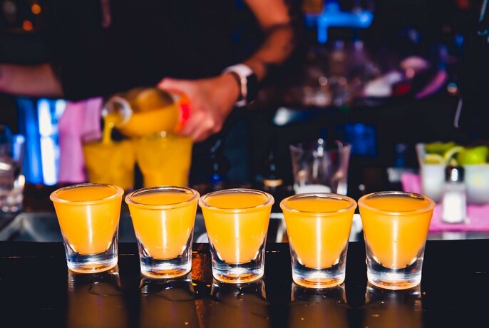 Five shots of an orange drink lined up on a bar.