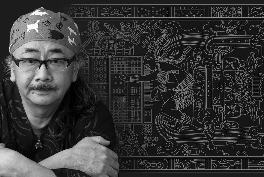 A black and white image of composer Nobuo Uematsu with a patterned fabric in the background. 