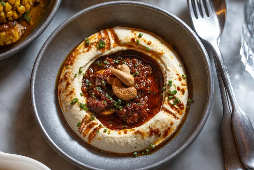 Looking down at a large plate of hummus, garnished with chilli oil,  cutlery alongside.