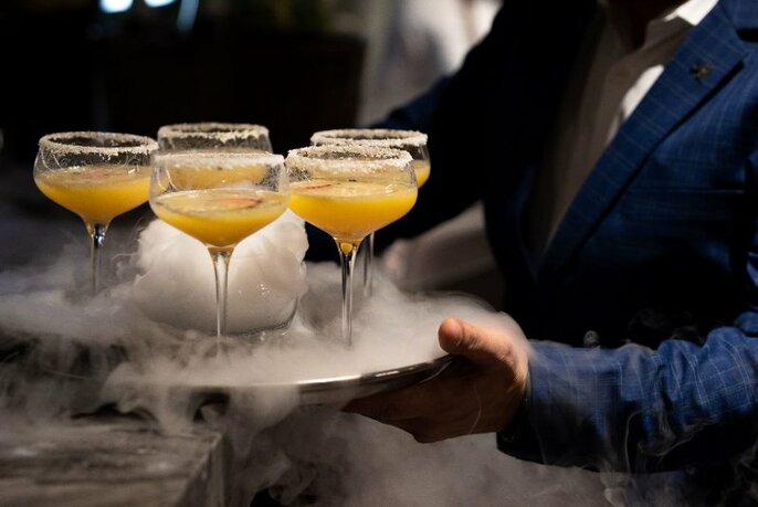 A waiter holding a tray of cocktails shrouded in dry ice.