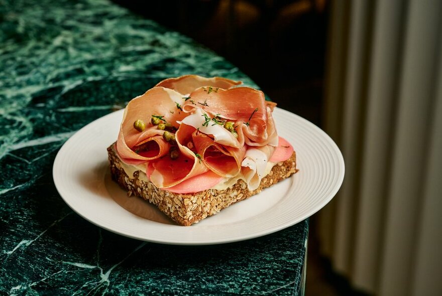 Cruled ham on thick slice of bread, on white plate on green marble-look surface.
