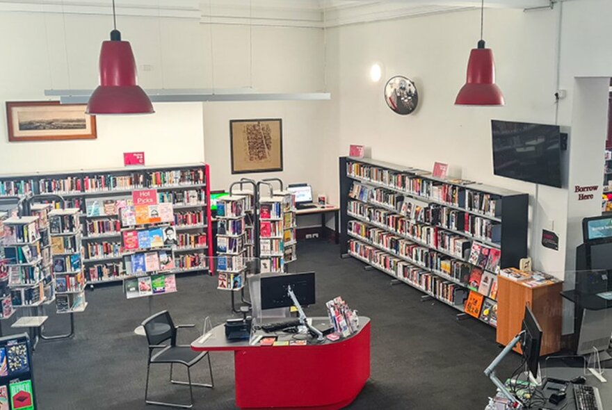 Aerial view of a large room at North Melbourne Library showing shelves of books against the walls and a customer service desk with a computer.
