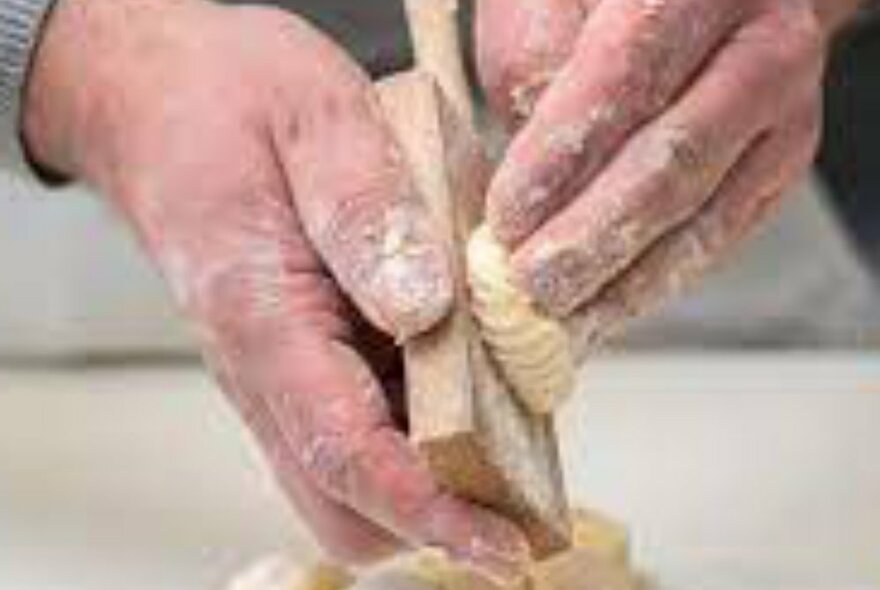 Floured hands making grooves in gnocchi using a wooded board. 
