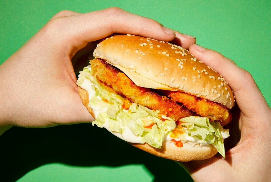 Hand holding chicken burger against green background.