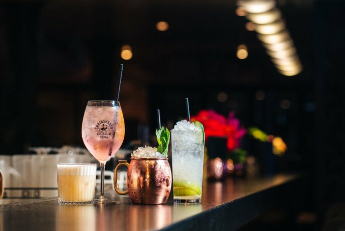 Four cocktails of varying kinds wait on a bar in a darkened space.