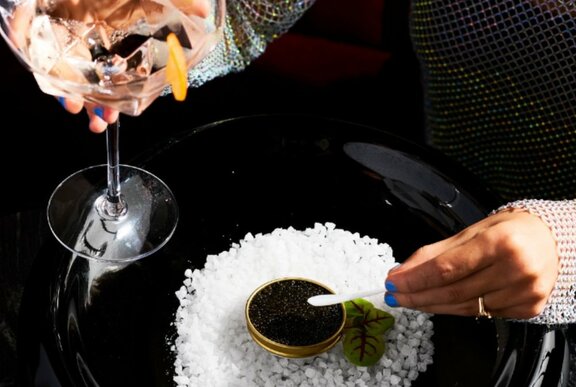 A Martini cocktail in a crystal glass alongside a dish of white salt rocks with a small amount of black caviar in the centre.