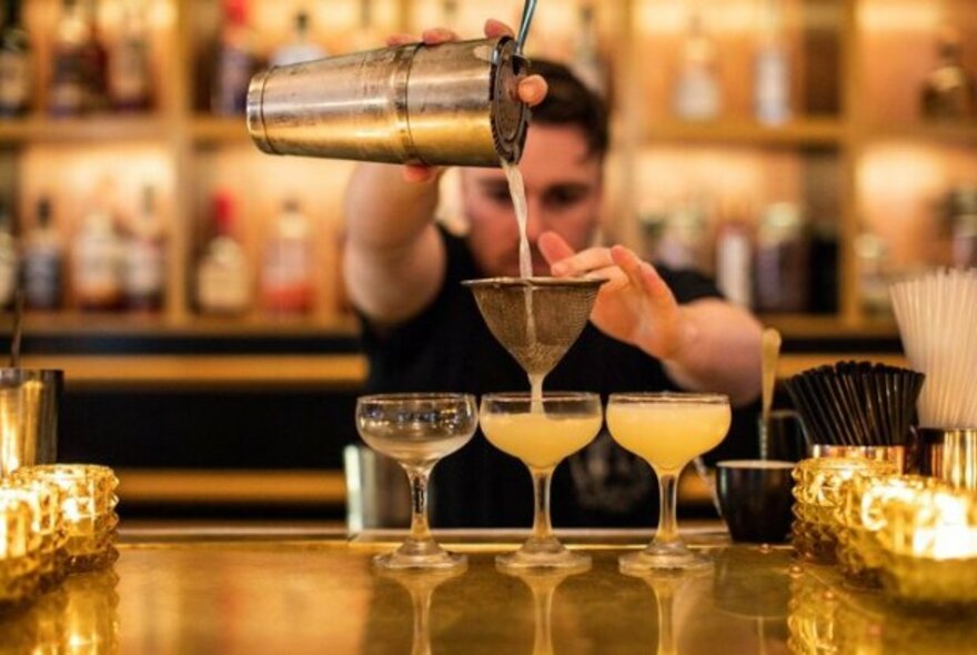 Bartender pouring yellow cocktails from a shaker.