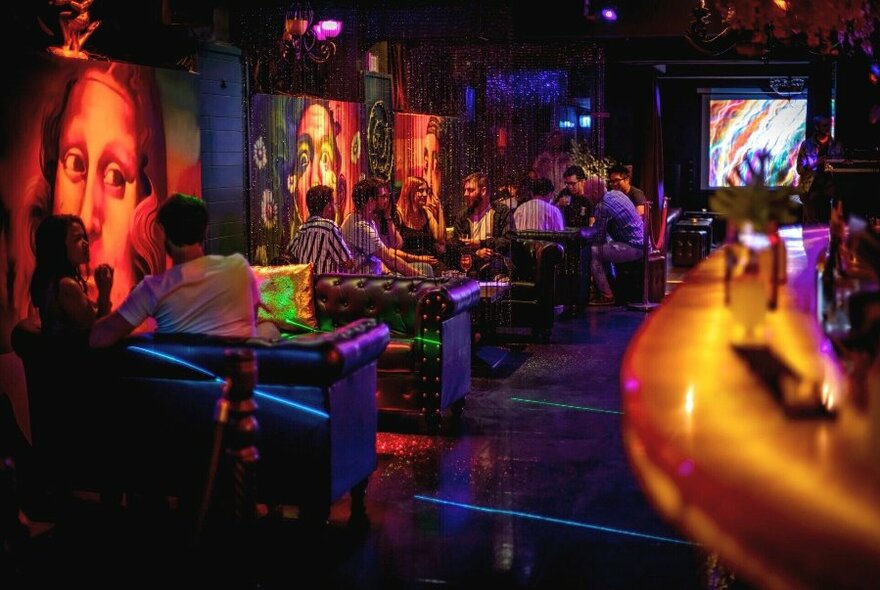 Interior of Miranda Bar with artwork on the walls, people sitting on leather lounges enjoying drinks, and a curved section of the bar visible in the right of the frame.
