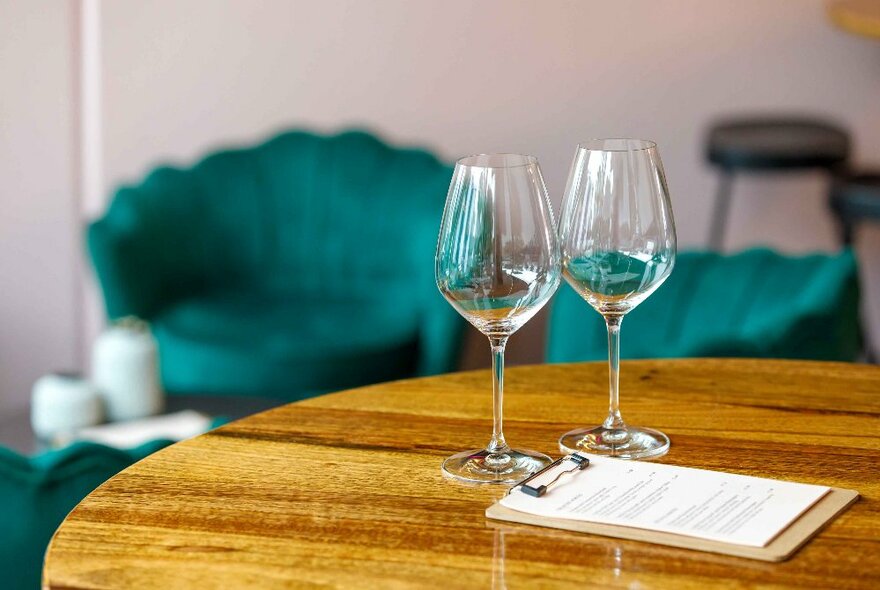 Two wine glasses on a round bar table with blue armchairs in the background.