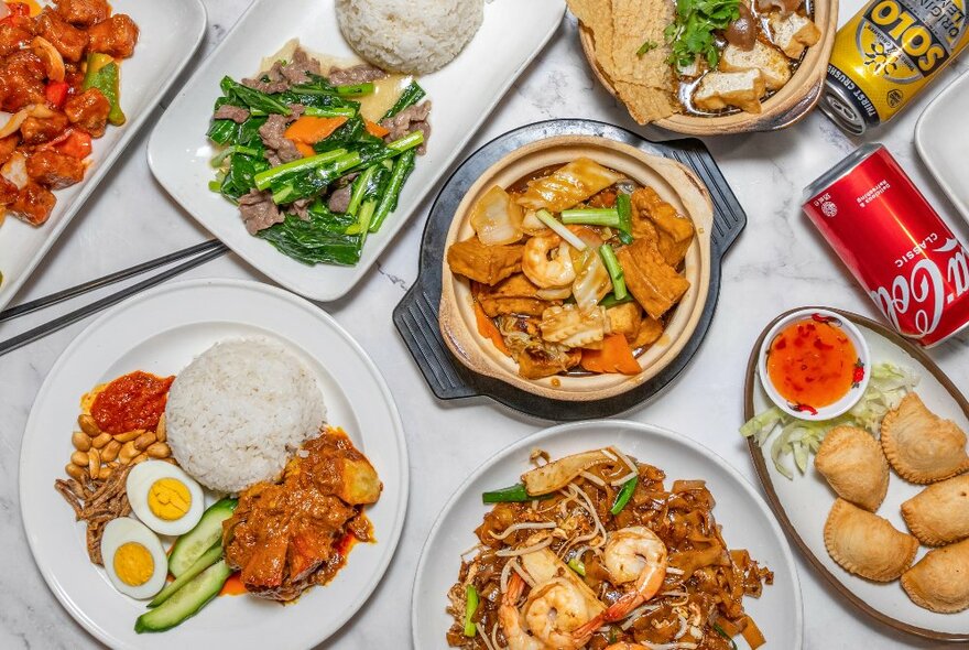 Looking down at a range of Malaysian and Chinese food on plates on a white table.