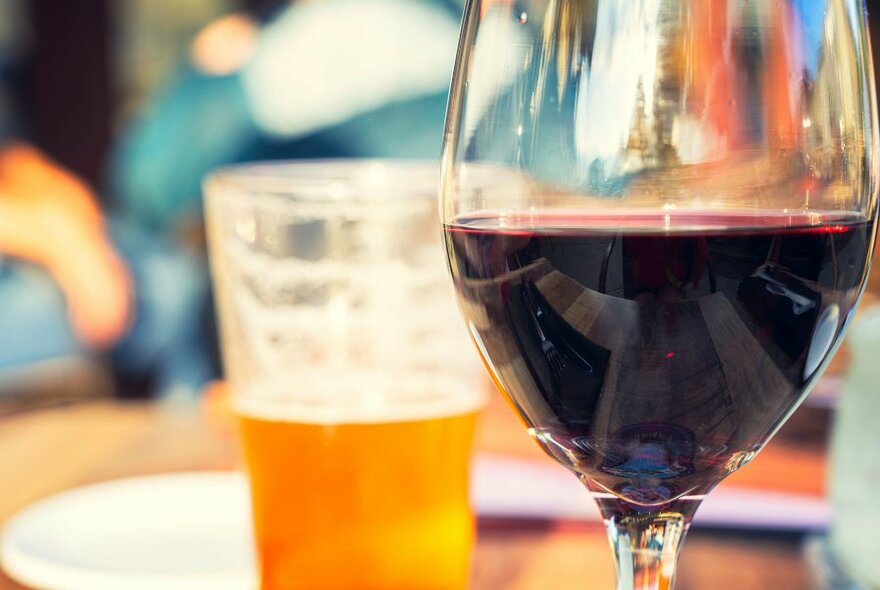 A close up of a glass of red wine with a beer in the background