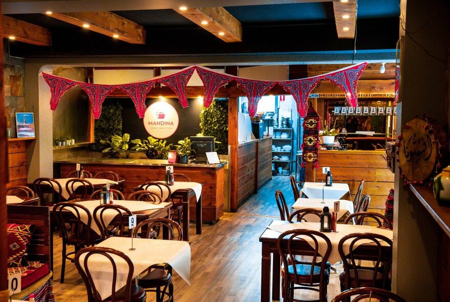 Cafe tables and chairs set for dinner in a wooden setting with overhead decorative fabric swags.