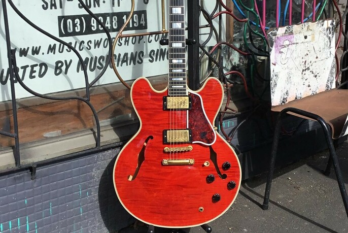 Red electric guitar resting on a stand outside the front of music swap shop.
