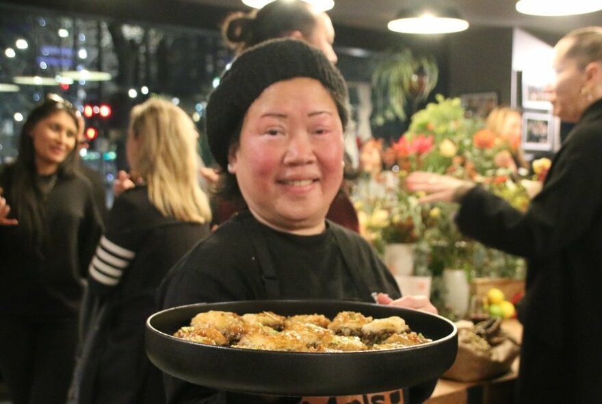 Smiling woman holding a platter of food out, people standing behind her.