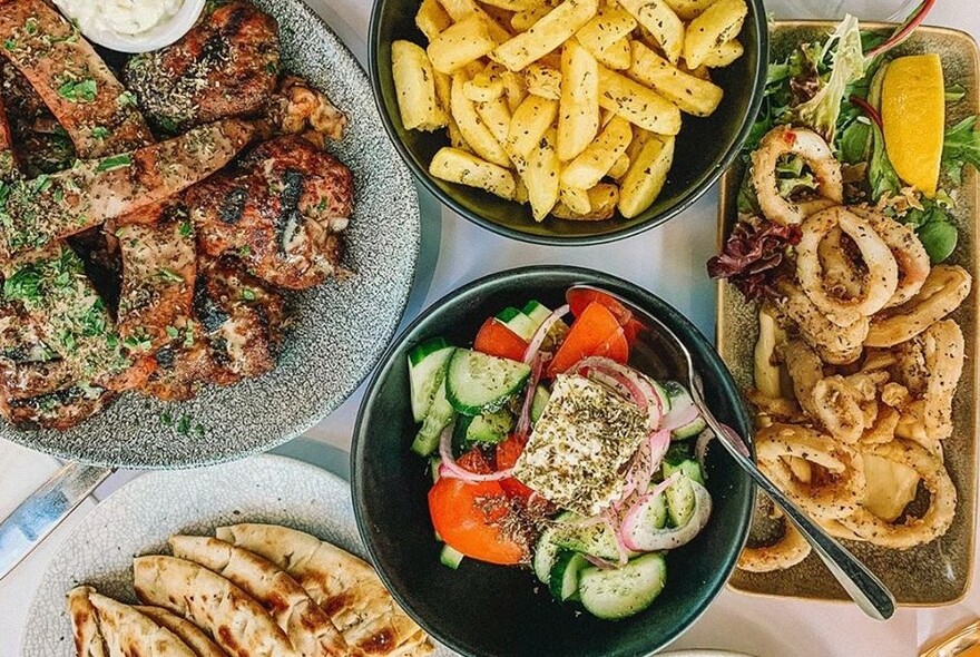 An assortment of Greek dishes including salad, calamari, bread and meat.