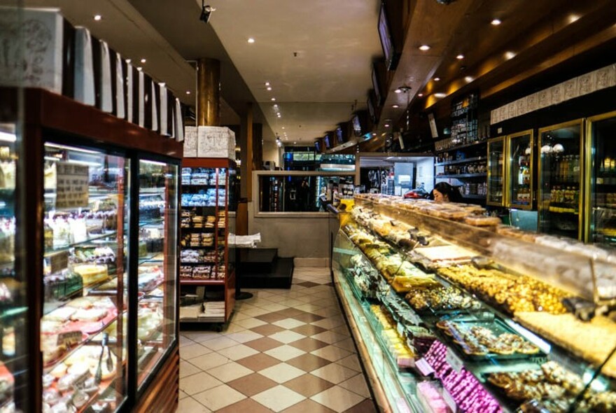 Shop interior with glass cabinets filled with cakes on the left and takeaway food on the right.