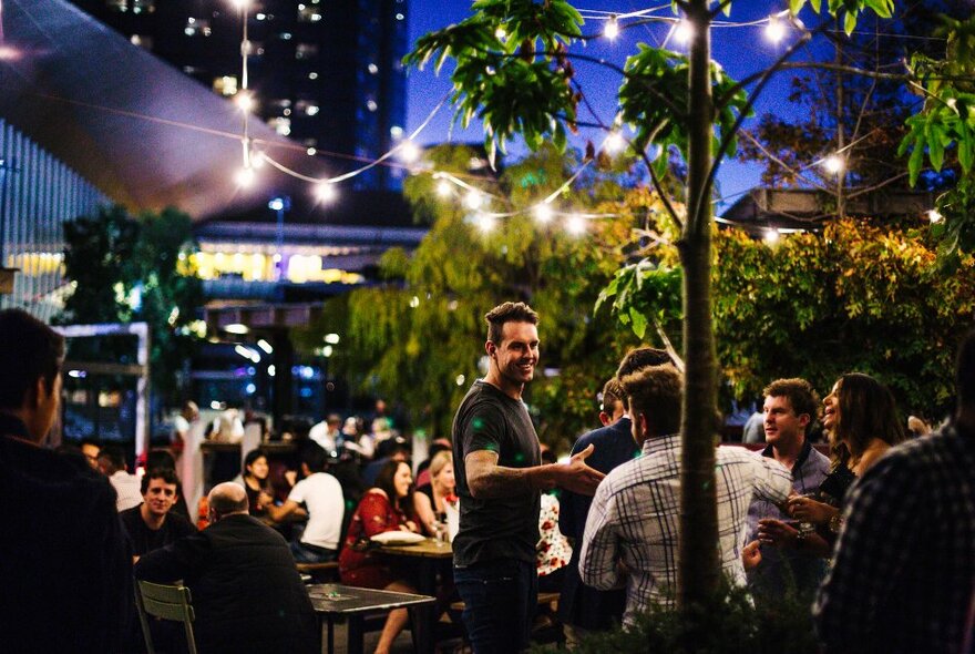 People seated at an outdoor bar with trees and lights.