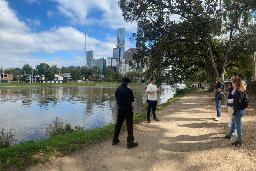 People gathered on the banks of the Yarra River, listening to a speaker, with the Melbourne city skyline in the background. 