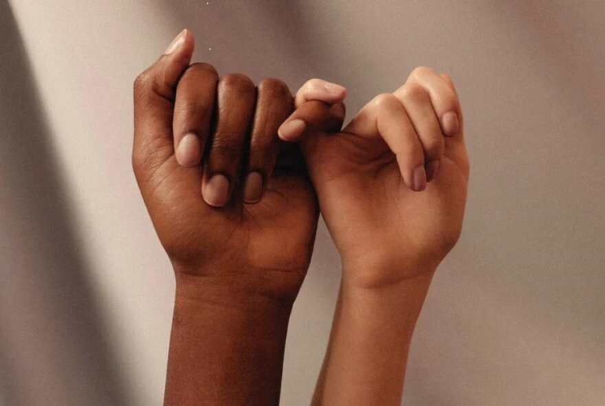 Two hands from different people raised in the air, with their pinky fingers intertwined.