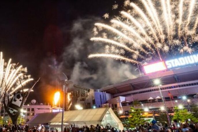 Fireworks exploding above the roof of Marvel Stadium with large crowds of onlookers watching underneath.