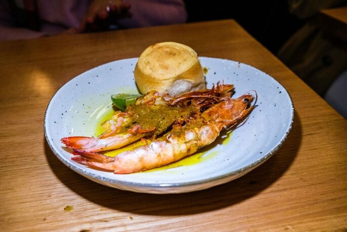 White plate of two grilled whole prawns and a side.
