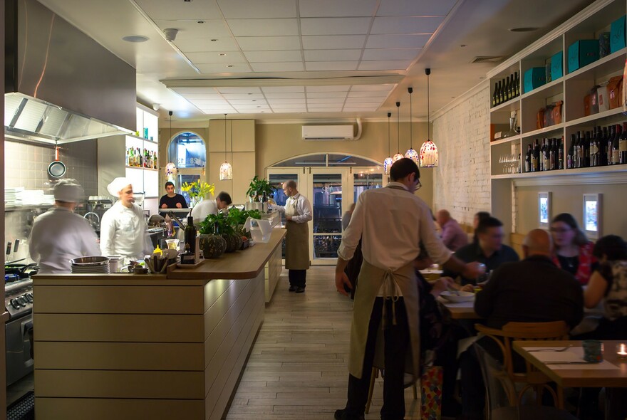 Restaurant interior with waiters and customers, chefs behind food station.